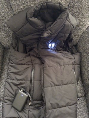 Insulated winter vest showing that it’s heated due to battery being shown out of its pocket and with the power lights being on